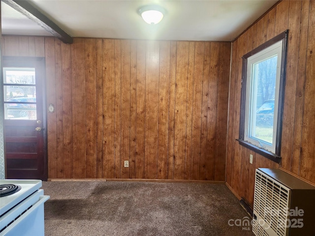 unfurnished dining area with wood walls, carpet flooring, beam ceiling, and heating unit