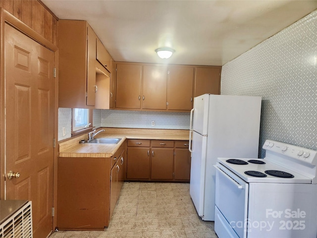 kitchen featuring tasteful backsplash, light countertops, a sink, white appliances, and wallpapered walls