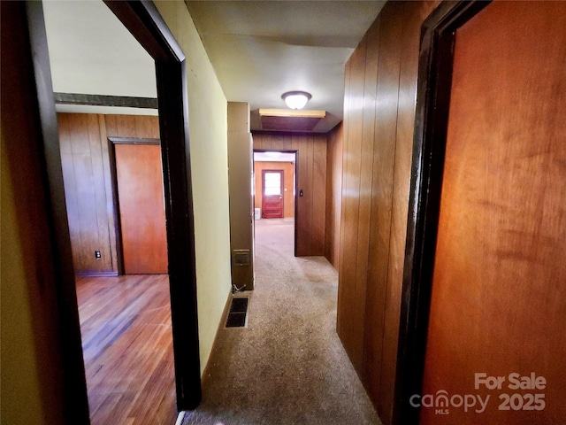 hall with carpet floors, visible vents, and wood walls