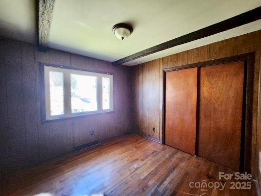 unfurnished bedroom with a closet, wood finished floors, and wooden walls