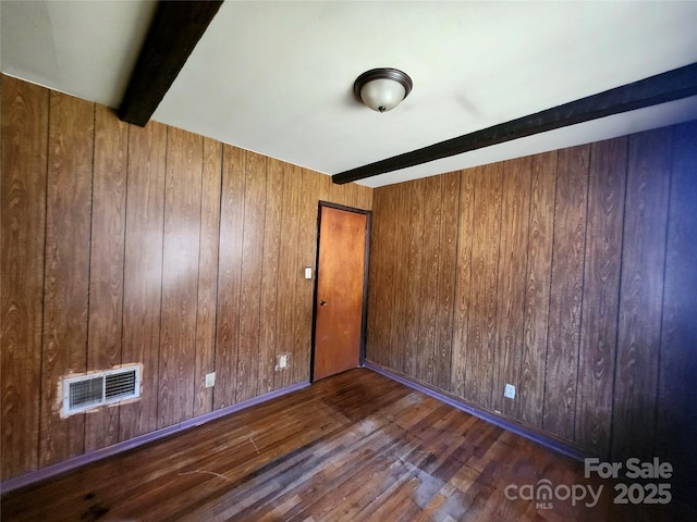 empty room with beam ceiling, wood-type flooring, visible vents, and wooden walls