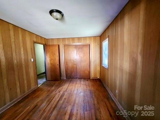 unfurnished bedroom with a closet, wood walls, and wood finished floors