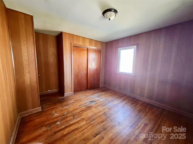 unfurnished bedroom with wooden walls, a closet, baseboards, and wood finished floors