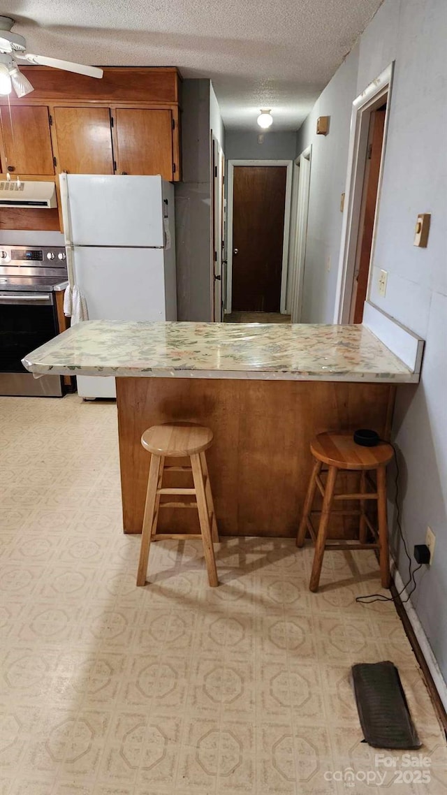 kitchen with white fridge, stainless steel range with electric stovetop, kitchen peninsula, and a breakfast bar area