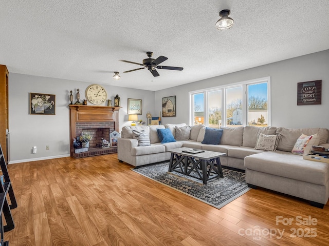 living room with a brick fireplace, hardwood / wood-style flooring, a textured ceiling, and ceiling fan