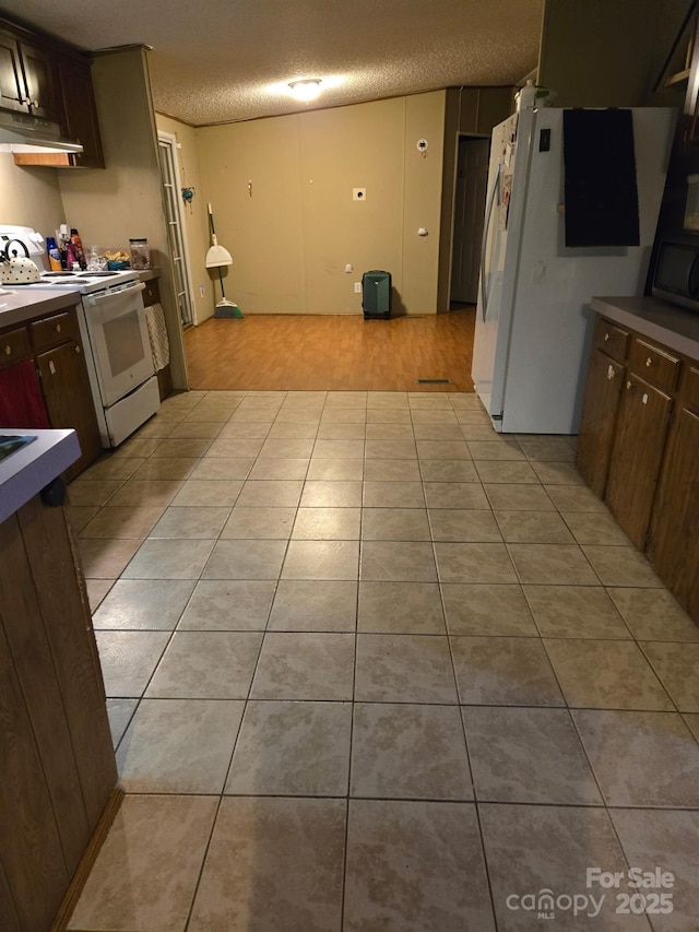 kitchen with white appliances, dark brown cabinetry, a textured ceiling, and light tile patterned floors