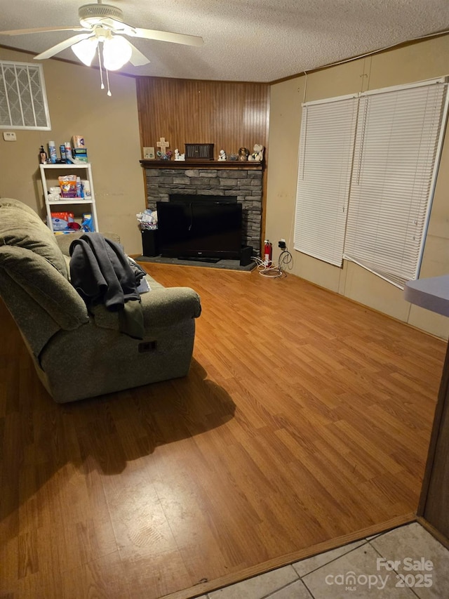 living room with hardwood / wood-style flooring, ceiling fan, a stone fireplace, and a textured ceiling