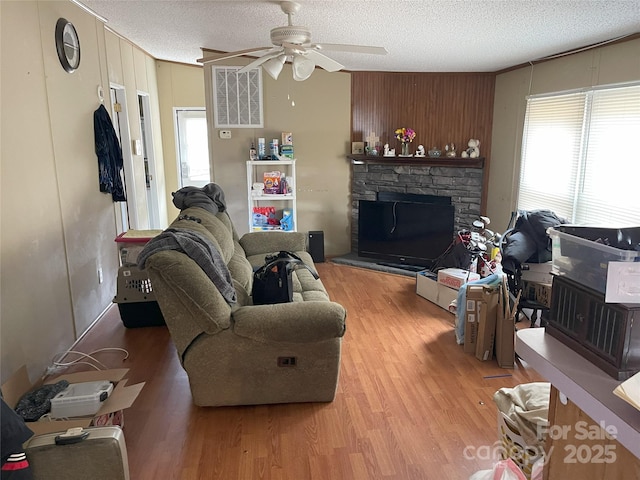 living room with ceiling fan, a fireplace, light hardwood / wood-style flooring, and a textured ceiling