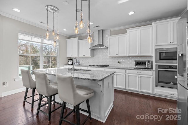 kitchen featuring white cabinetry, wall chimney range hood, stainless steel appliances, and a center island with sink