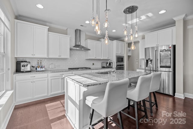 kitchen featuring a kitchen island with sink, white cabinets, stainless steel appliances, and wall chimney exhaust hood