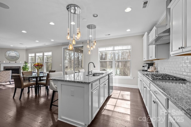 kitchen with sink, wall chimney range hood, appliances with stainless steel finishes, white cabinetry, and a center island with sink