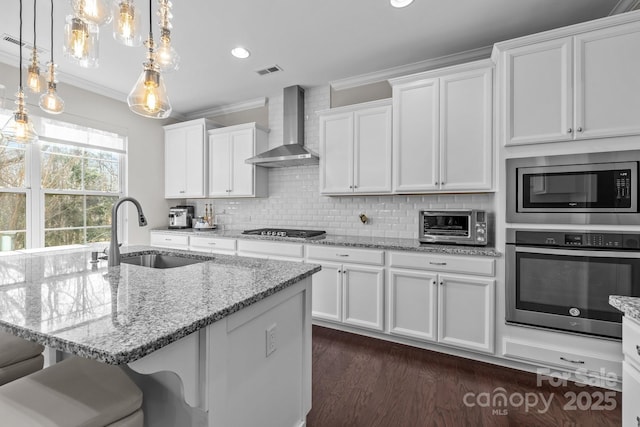 kitchen featuring pendant lighting, white cabinetry, sink, stainless steel appliances, and wall chimney exhaust hood