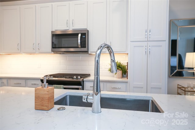 kitchen featuring stainless steel appliances, white cabinets, and light stone counters