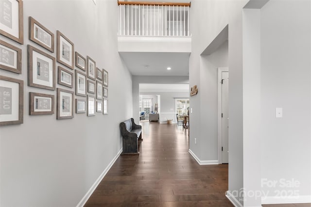 corridor with a towering ceiling, dark wood-style floors, baseboards, and recessed lighting