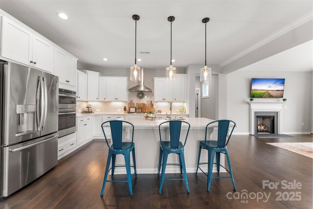 kitchen with white cabinets, wall chimney exhaust hood, appliances with stainless steel finishes, and light countertops