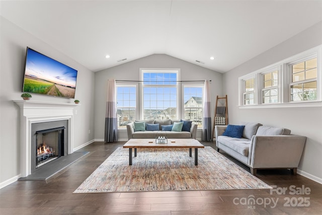 living area featuring a warm lit fireplace, dark wood-type flooring, visible vents, baseboards, and vaulted ceiling