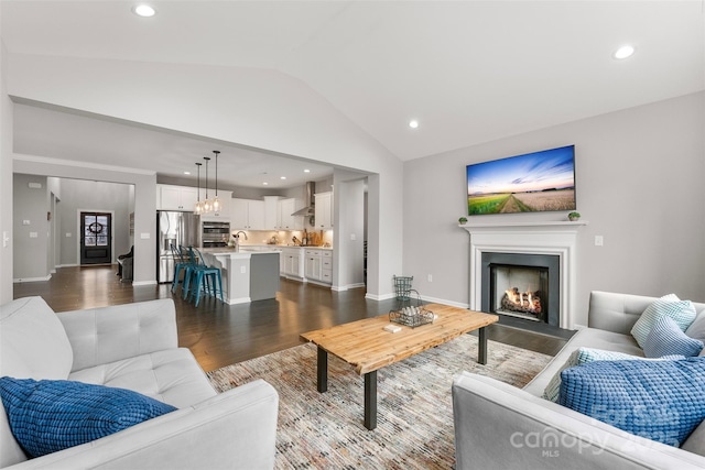 living room featuring recessed lighting, vaulted ceiling, wood finished floors, a lit fireplace, and baseboards