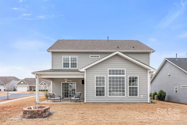 back of house with a ceiling fan, an outdoor fire pit, roof with shingles, and a patio