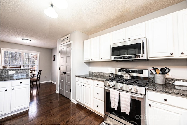 kitchen featuring white cabinetry, stainless steel appliances, and dark stone counters