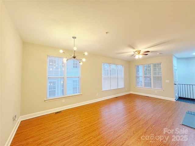 empty room with ceiling fan with notable chandelier and light hardwood / wood-style flooring