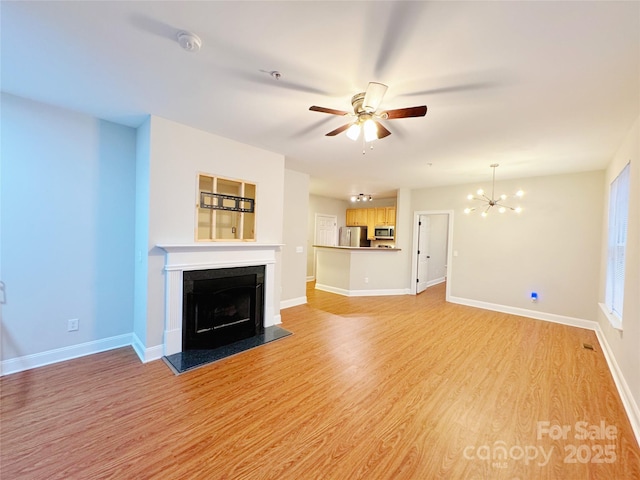 unfurnished living room with ceiling fan with notable chandelier, a fireplace, and light wood-type flooring