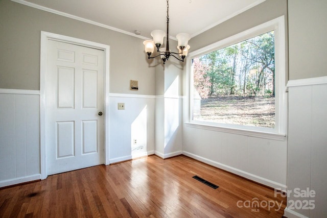 unfurnished dining area with ornamental molding, hardwood / wood-style floors, and an inviting chandelier