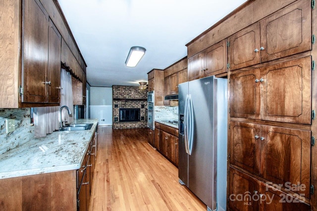 kitchen featuring sink, light hardwood / wood-style flooring, appliances with stainless steel finishes, tasteful backsplash, and a brick fireplace