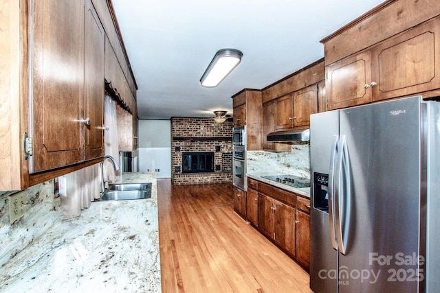 kitchen with sink, backsplash, stainless steel appliances, a brick fireplace, and light wood-type flooring