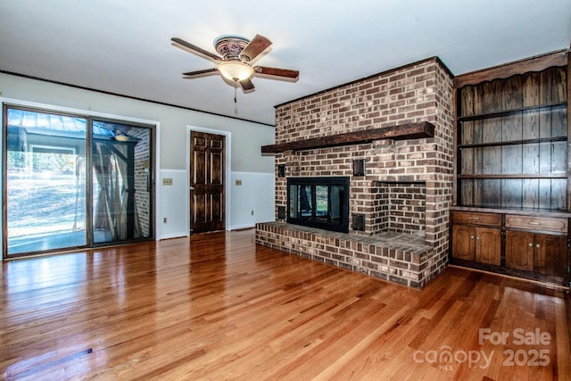 unfurnished living room with ceiling fan, a fireplace, and light wood-type flooring