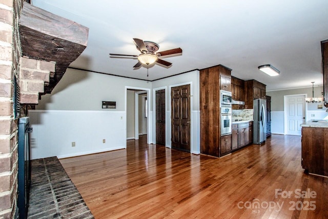 unfurnished living room featuring ornamental molding, ceiling fan with notable chandelier, and dark hardwood / wood-style flooring