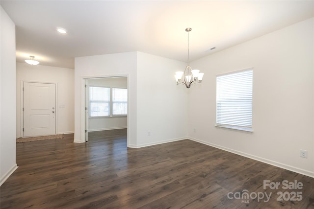 empty room with dark wood-type flooring and a chandelier