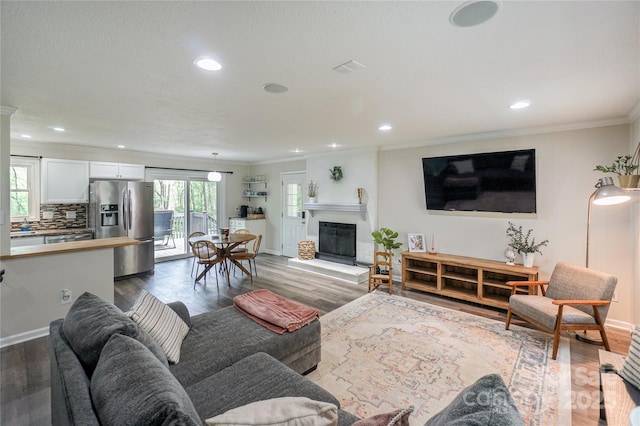 living area featuring dark wood-style flooring, ornamental molding, a glass covered fireplace, and recessed lighting