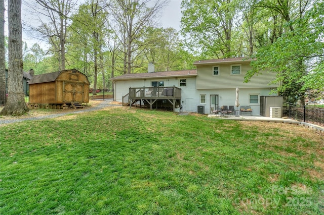 back of property with a wooden deck, an outbuilding, fence, a lawn, and a storage unit