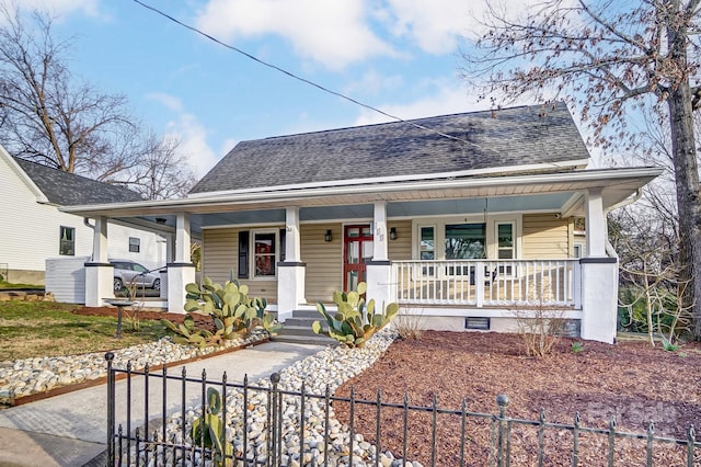 view of front facade featuring covered porch, a shingled roof, and a fenced front yard