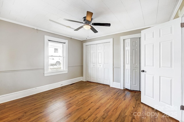 unfurnished bedroom with wood finished floors, crown molding, baseboards, and two closets