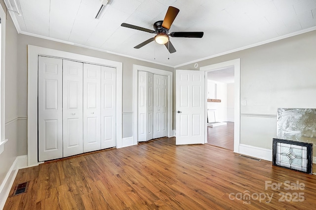 unfurnished bedroom featuring multiple closets, visible vents, crown molding, and wood finished floors