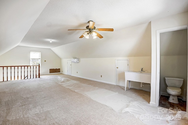 additional living space featuring lofted ceiling, a textured ceiling, light carpet, baseboards, and a wall mounted AC