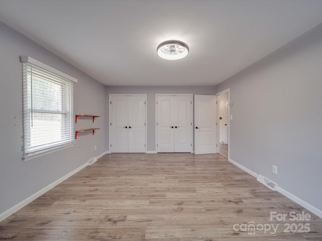 unfurnished bedroom with light hardwood / wood-style flooring and two closets