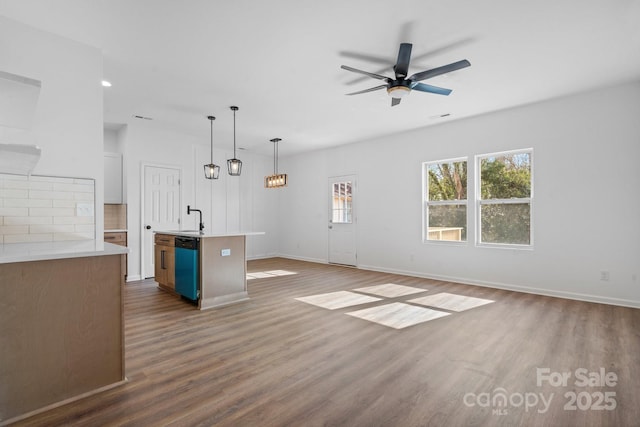 interior space with pendant lighting, dishwasher, sink, dark hardwood / wood-style flooring, and a kitchen island with sink