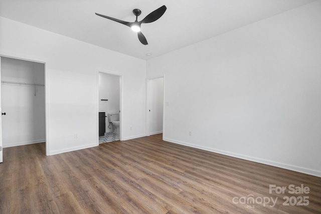 unfurnished bedroom with ceiling fan, ensuite bathroom, wood-type flooring, a spacious closet, and a closet