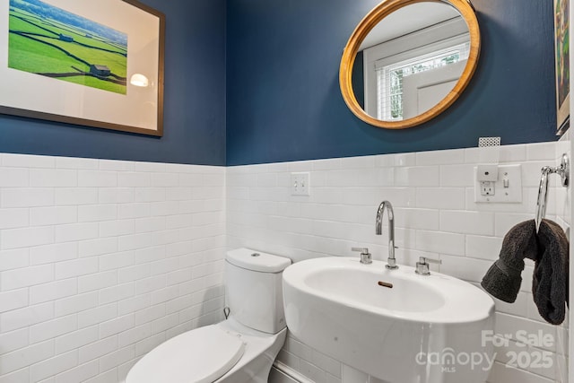 bathroom with toilet, sink, and tile walls