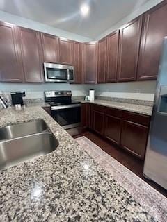 kitchen with stainless steel appliances, sink, dark brown cabinetry, and light stone counters