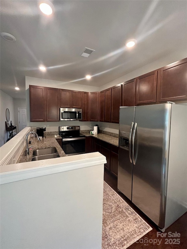 kitchen with appliances with stainless steel finishes, sink, dark brown cabinets, and kitchen peninsula