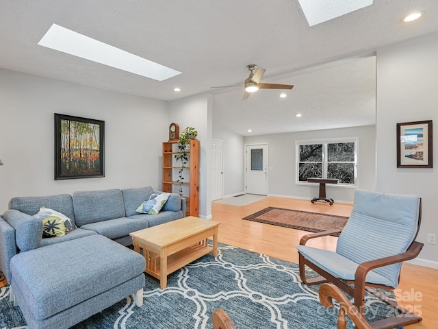 living room with light hardwood / wood-style flooring, a textured ceiling, a skylight, and ceiling fan