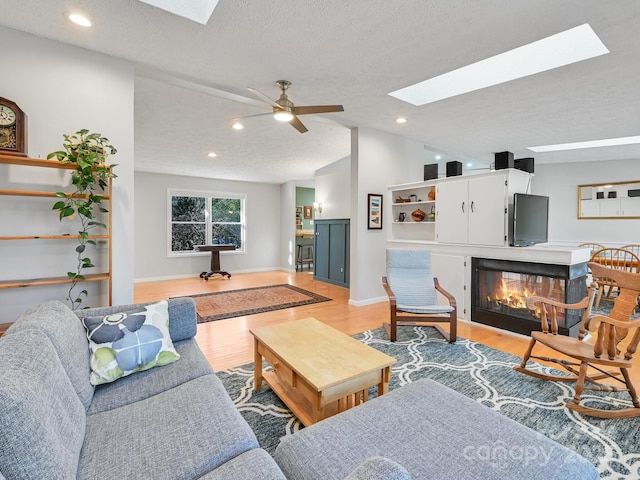 living room with ceiling fan, lofted ceiling with skylight, light hardwood / wood-style floors, and a textured ceiling