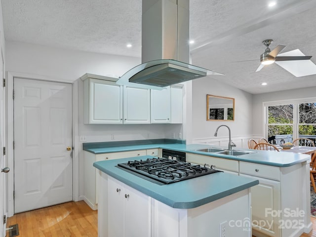 kitchen with a kitchen island, island range hood, sink, white cabinets, and stainless steel gas cooktop