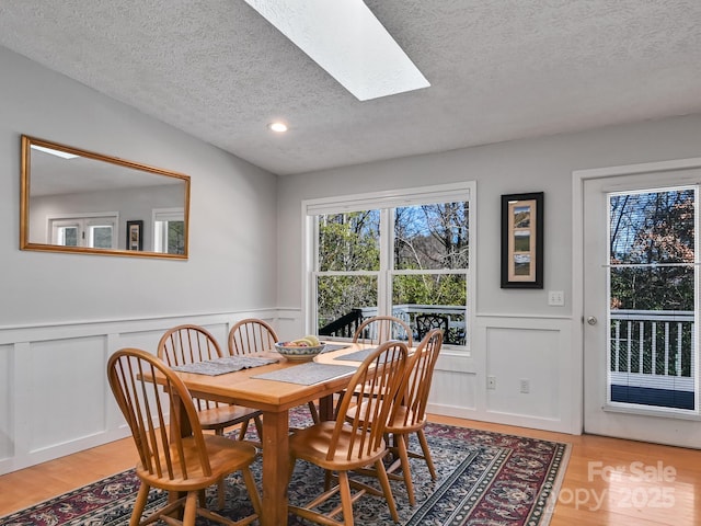 dining room with hardwood / wood-style flooring, a skylight, and a textured ceiling