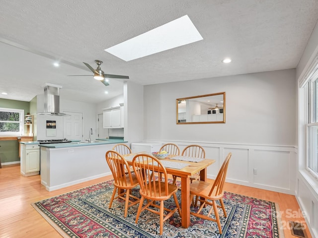 dining room featuring ceiling fan, lofted ceiling with skylight, light hardwood / wood-style floors, and a textured ceiling