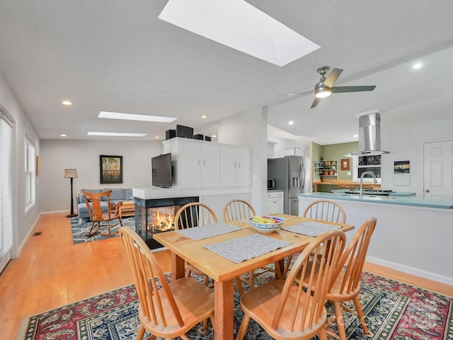 dining room with ceiling fan, a skylight, light hardwood / wood-style floors, and a textured ceiling