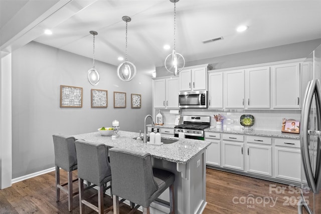 kitchen featuring sink, white cabinetry, stainless steel appliances, a center island with sink, and decorative light fixtures